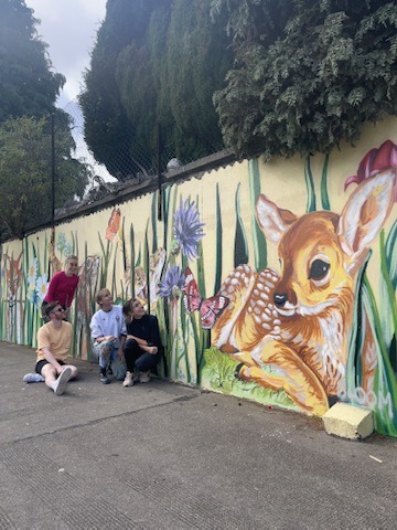 Children sitting in front of a fawn and flower mural on an outdoor wall